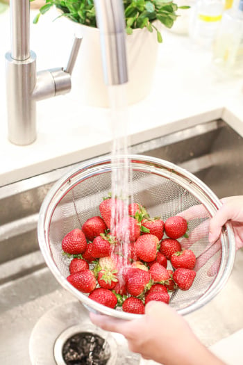 strawberries being rinsed in a strainer